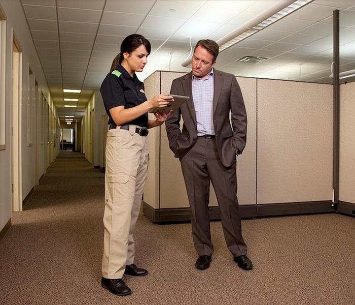 a SERVPRO employee standing in an office next to a person reviewing plans